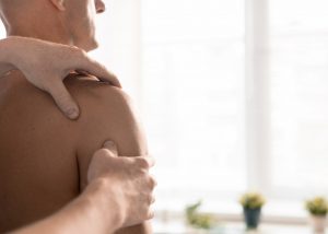 Hands of professional masseur or physiotherapist massaging shoulder of man